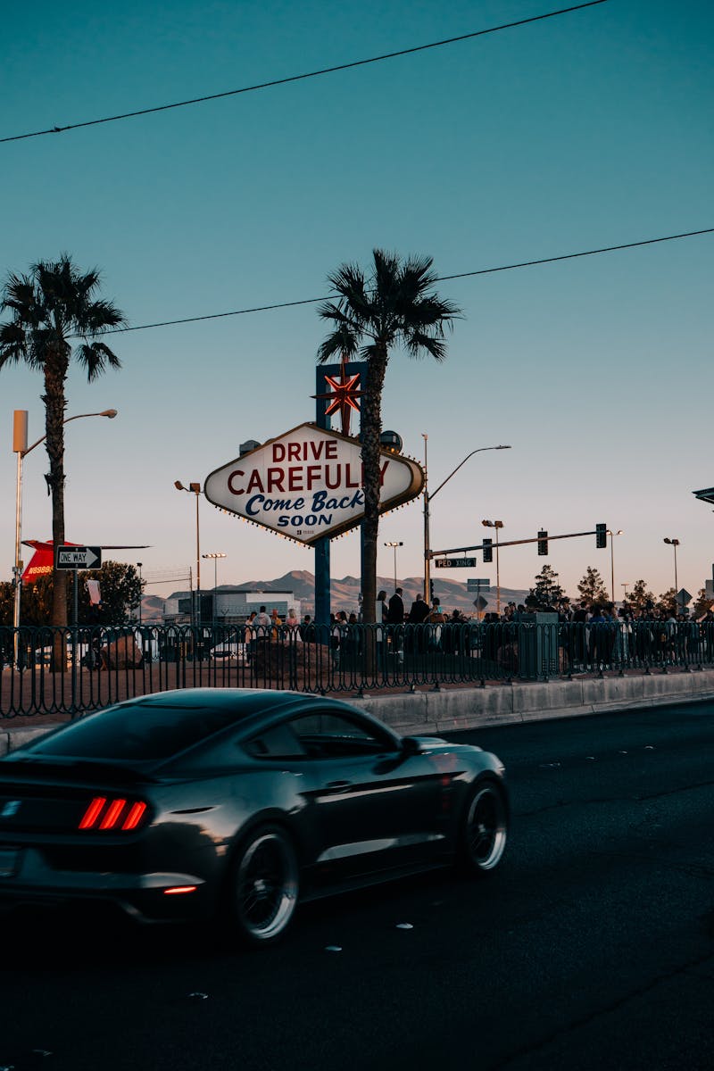 Black Car on a Highway and Palm Trees against Sky at Dusk