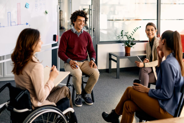 Group of people, one in a wheelchair, discussing work in a white room