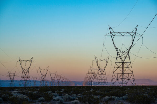 The silhouette of a power transmission line vanishing into a point in the distance during sunset.