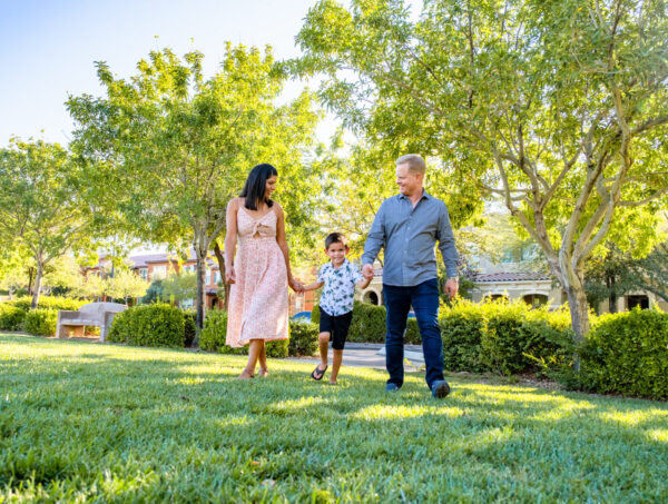 A man and a woman holding hands with a child walking through the grass.