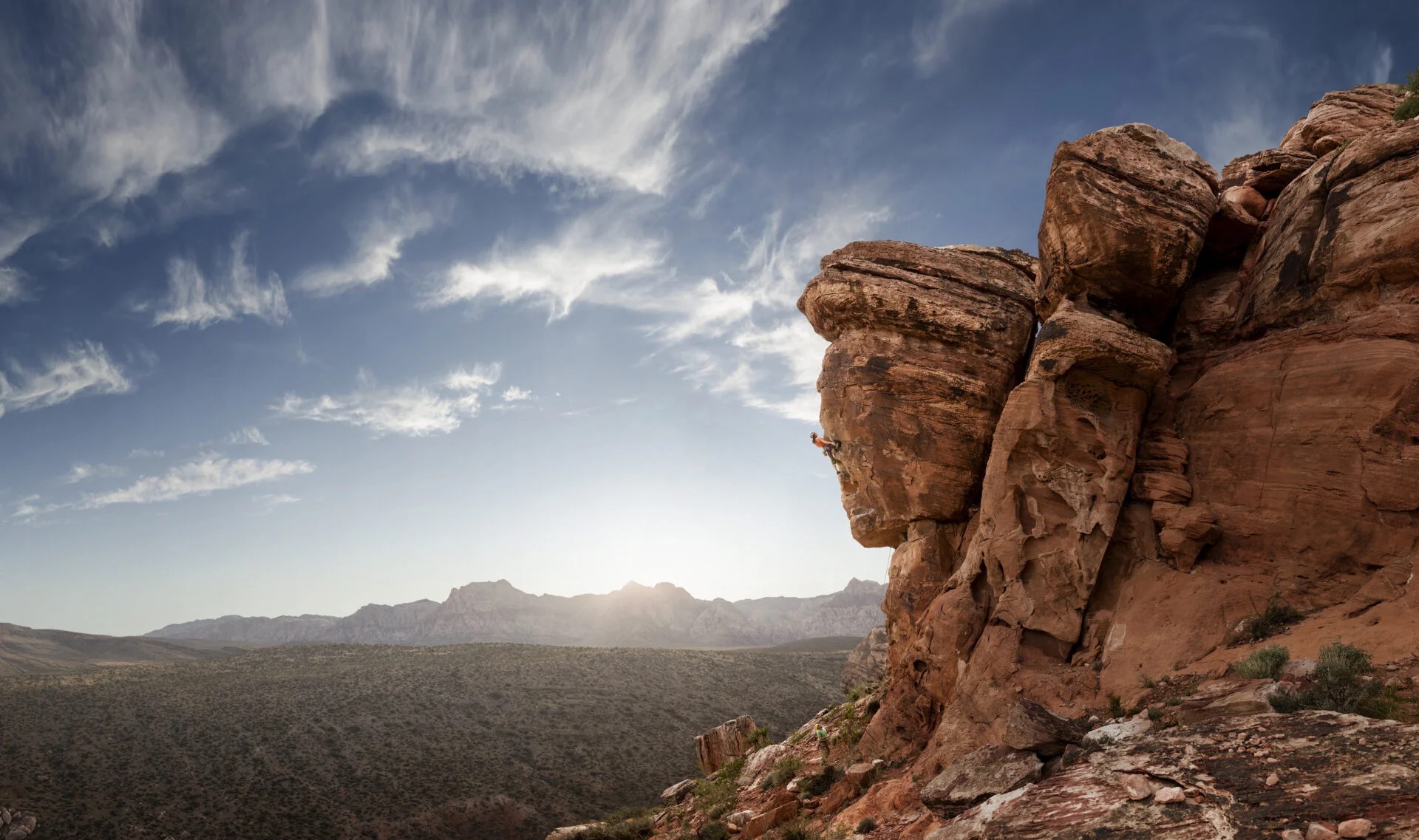 Stunning blue skies behind a rock overhang with a rock climber halfway up.