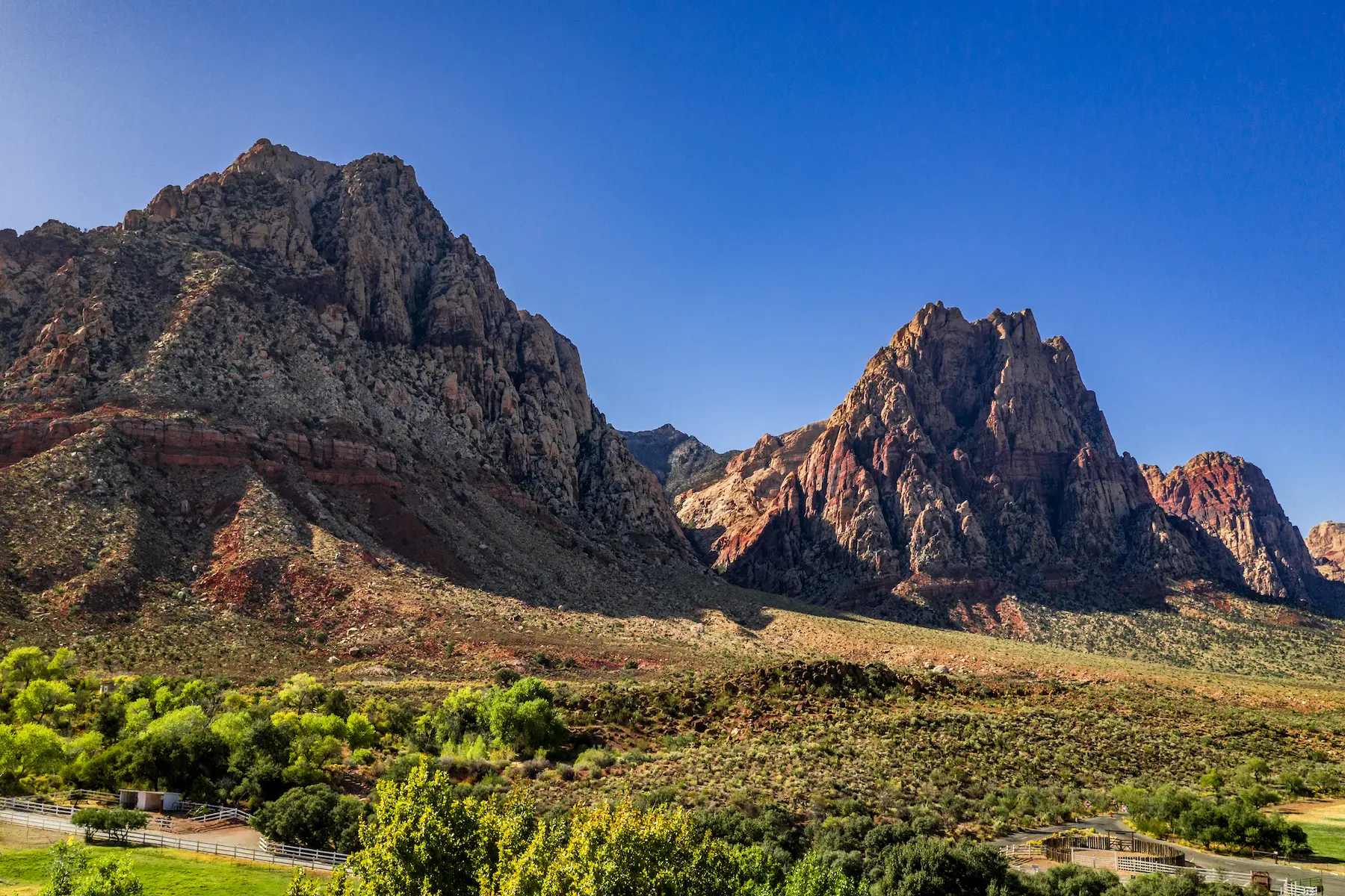 Beautiful view of famous Spring Mountain Ranch State Park near Las Vegas and Red Rock Canyon, Nevada during autumn with pink and red rock mountains, blue sky, green trees and grass, and purple hills