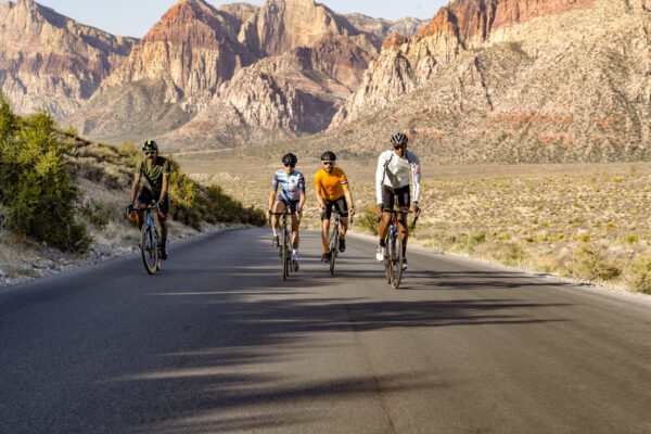 Four people riding a bike through Red Rock Canyon on a paved road