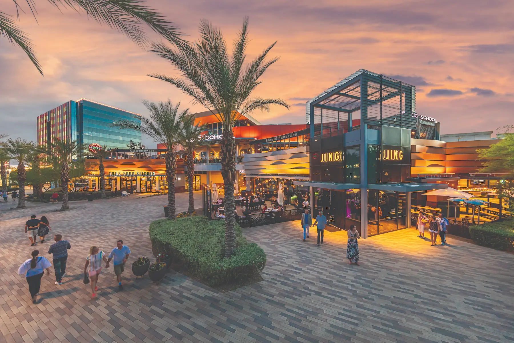 Downtown Summerlin at sunset, featuring a modern Las Vegas shopping and dining district lined with palm trees and a decorative fountain in the center.