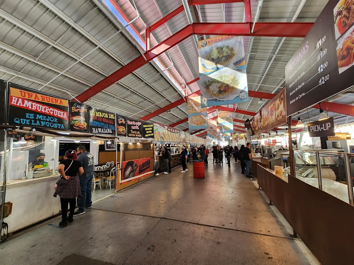 Broadacres Marketplace – An indoor market with red steel beams, food stalls, and people browsing under a metal roof.