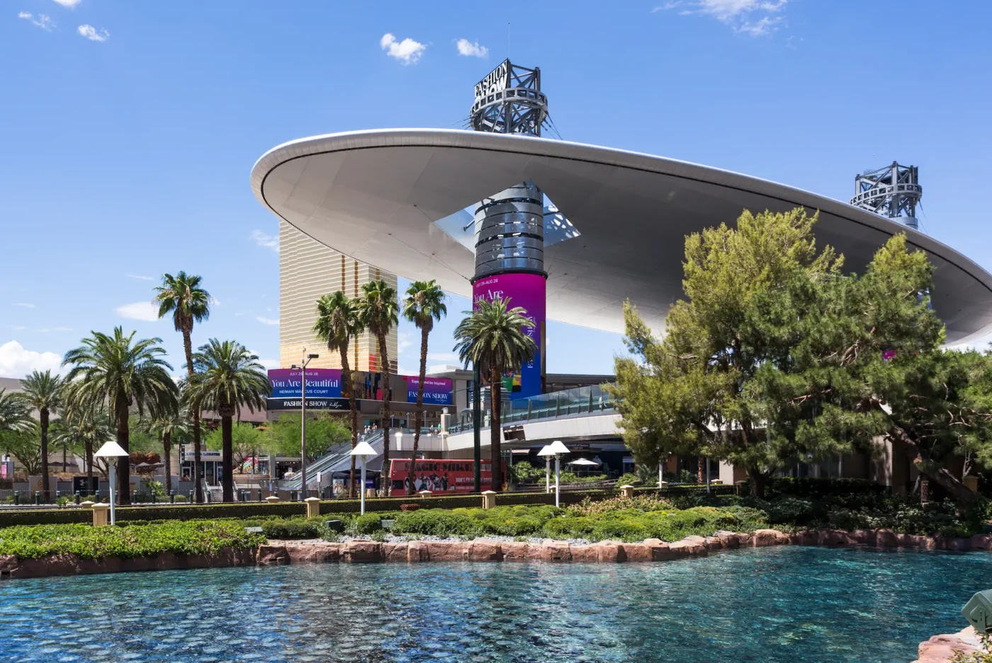 Fashion Show Mall in Las Vegas, showcasing its distinctive UFO-shaped canopy and reflecting pool, with luxury shops and palm trees in the background.